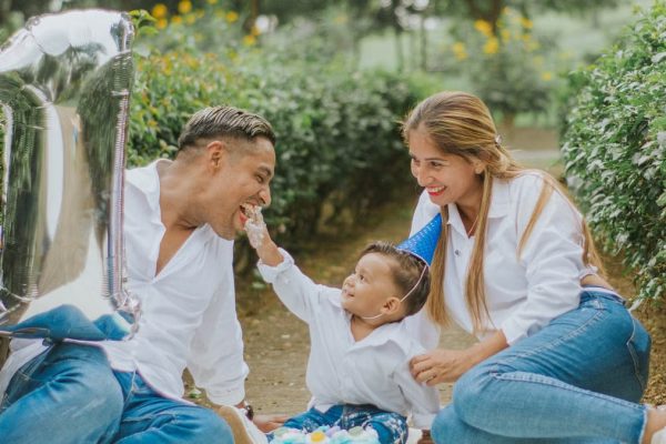 A joyful family celebrating their child's first birthday outdoors with cake and balloons.